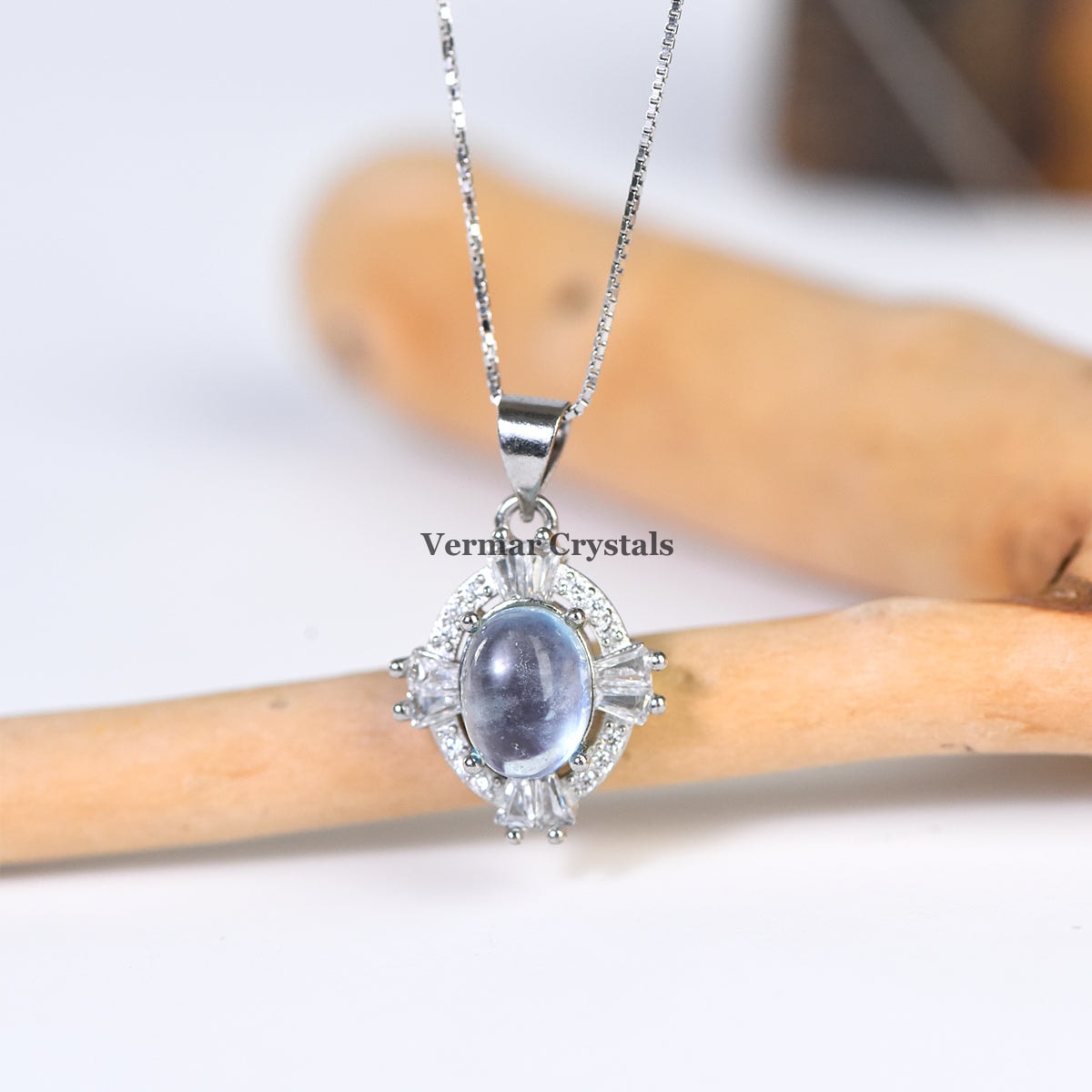 Elegant silver pendant necklace with oval aquamarine blue stone and sparkling clear crystals on natural wood background