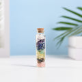 Mini glass vial filled with layered natural crystal chips and sealed with a cork on white surface with soft background