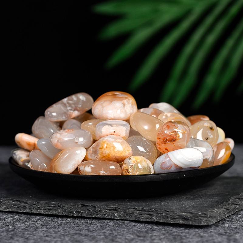 Smooth polished carnelian stones with warm orange and white hues displayed on a black dish against dark background