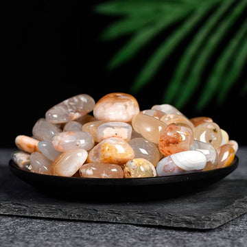 Smooth polished carnelian stones with warm orange and white hues displayed on a black dish against dark background