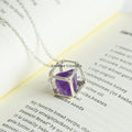 Handcrafted amethyst raw crystal pendant wire wrapped in silver wire on a delicate chain resting on an open book page