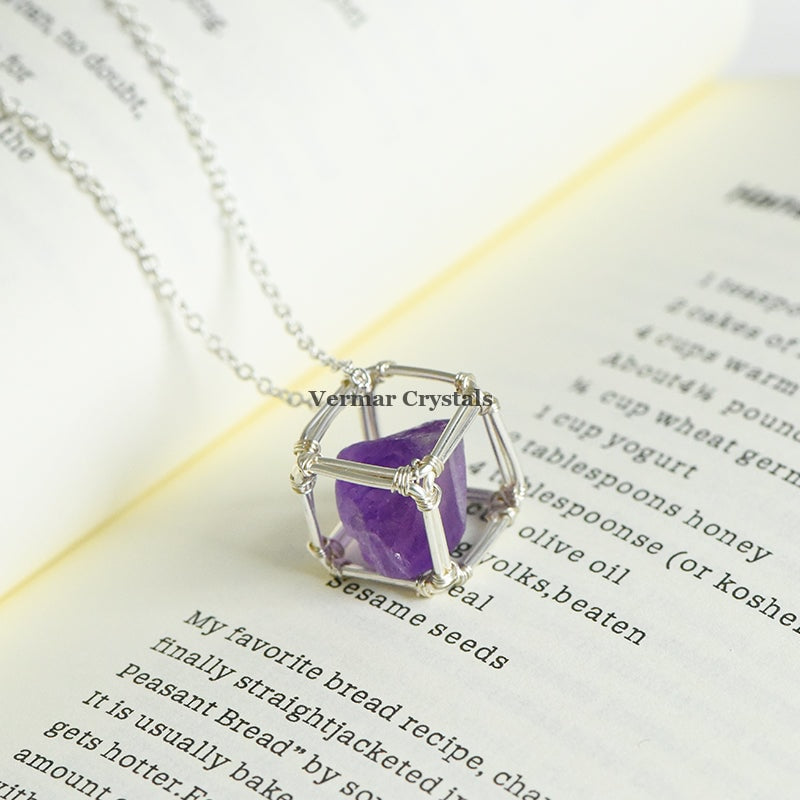 Handcrafted amethyst raw crystal pendant wire wrapped in silver wire on a delicate chain resting on an open book page