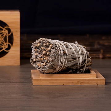 Rolled bundle of dried white sage leaves tied with string resting on a small wooden tray on dark surface