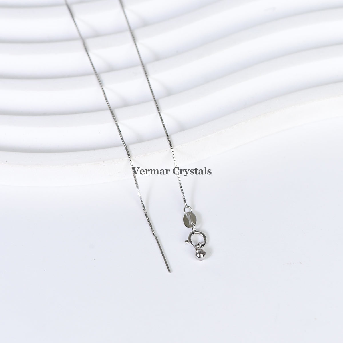 Delicate silver chain necklace with lobster clasp and small oval tag on white textured background