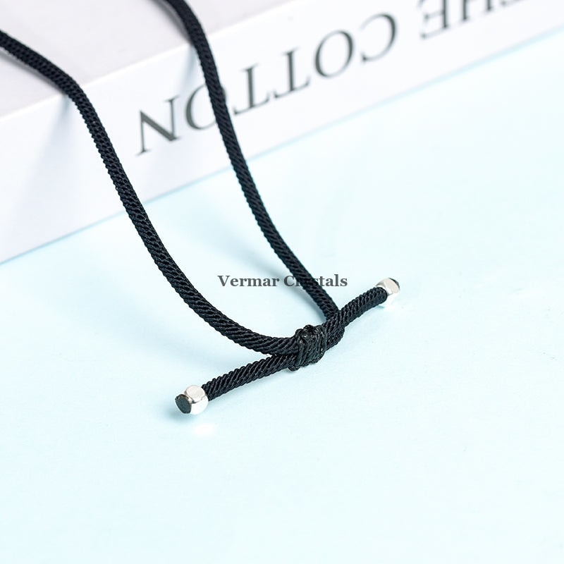 Close-up of black cord with silver end caps and adjustable woven knot on light blue surface with blurred book background