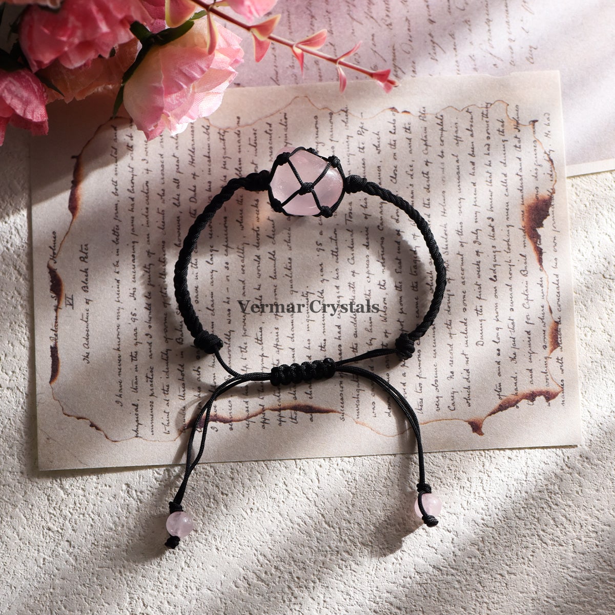 Handmade black cord bracelet with net-wrapped natural tumbled rose quartz stone on vintage paper background