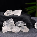 Natural clear quartz stones arranged on a dark fabric with a blurred green plant in the background