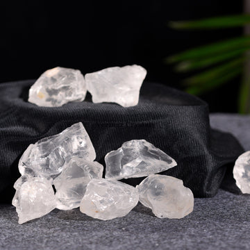 Natural clear quartz stones arranged on a dark fabric with a blurred green plant in the background