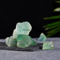 Natural green fluorite crystal stones with translucent, irregular shapes displayed on a dark stone slab