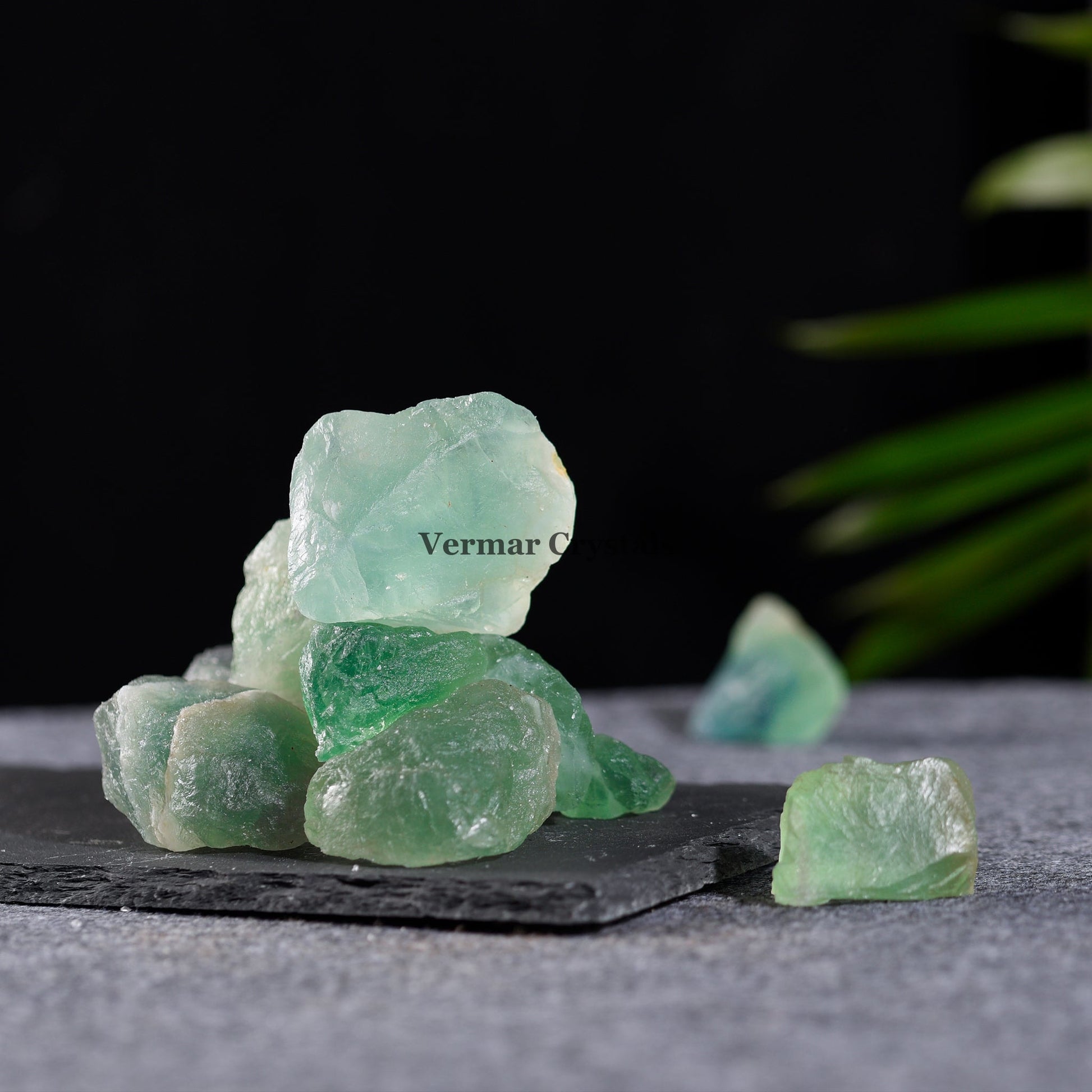 Natural green fluorite crystal stones with translucent, irregular shapes displayed on a dark stone slab