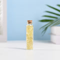 Mini glass vial filled with yellow citrine crystal chips sealed with natural cork on white surface with blurred background