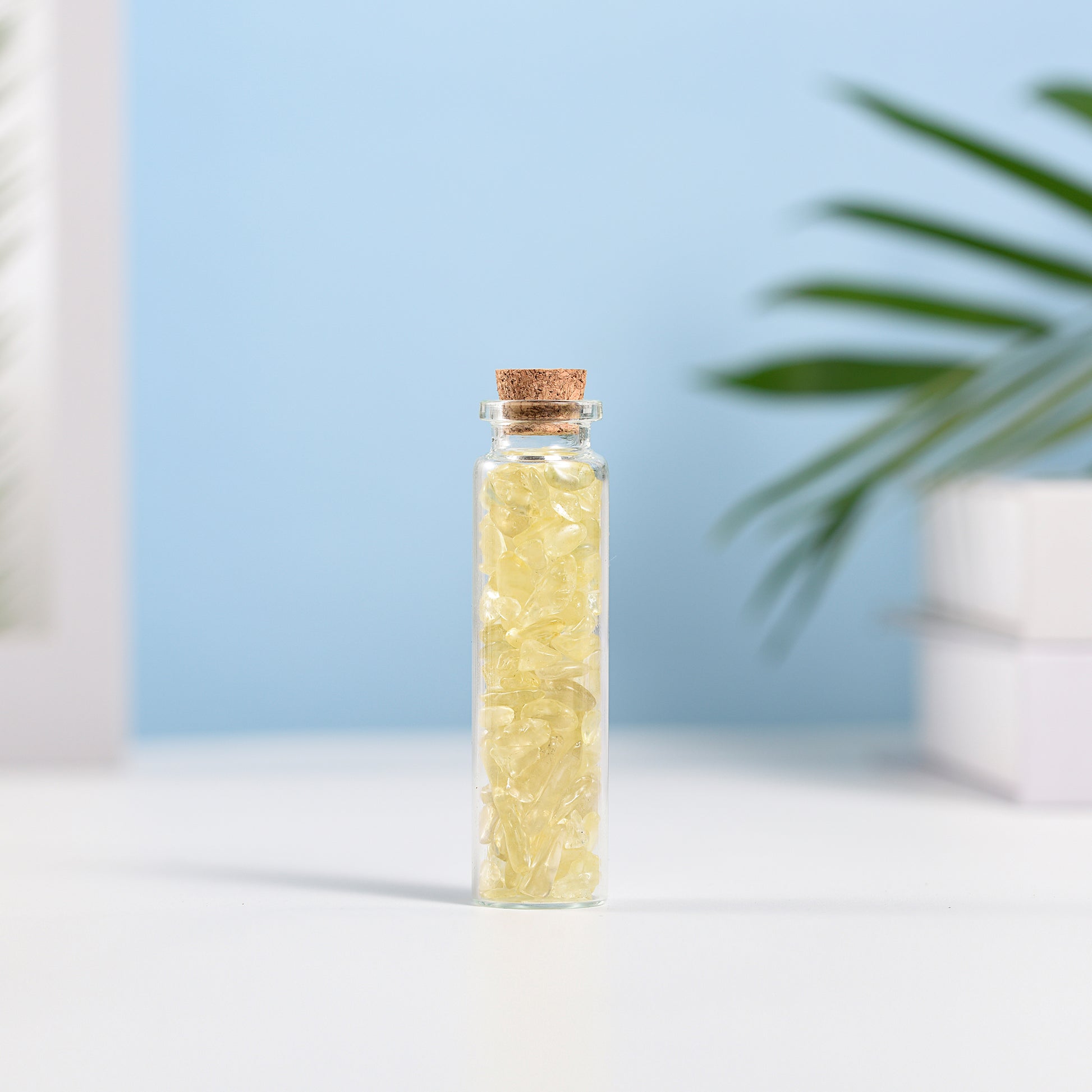 Mini glass vial filled with yellow citrine crystal chips sealed with natural cork on white surface with blurred background