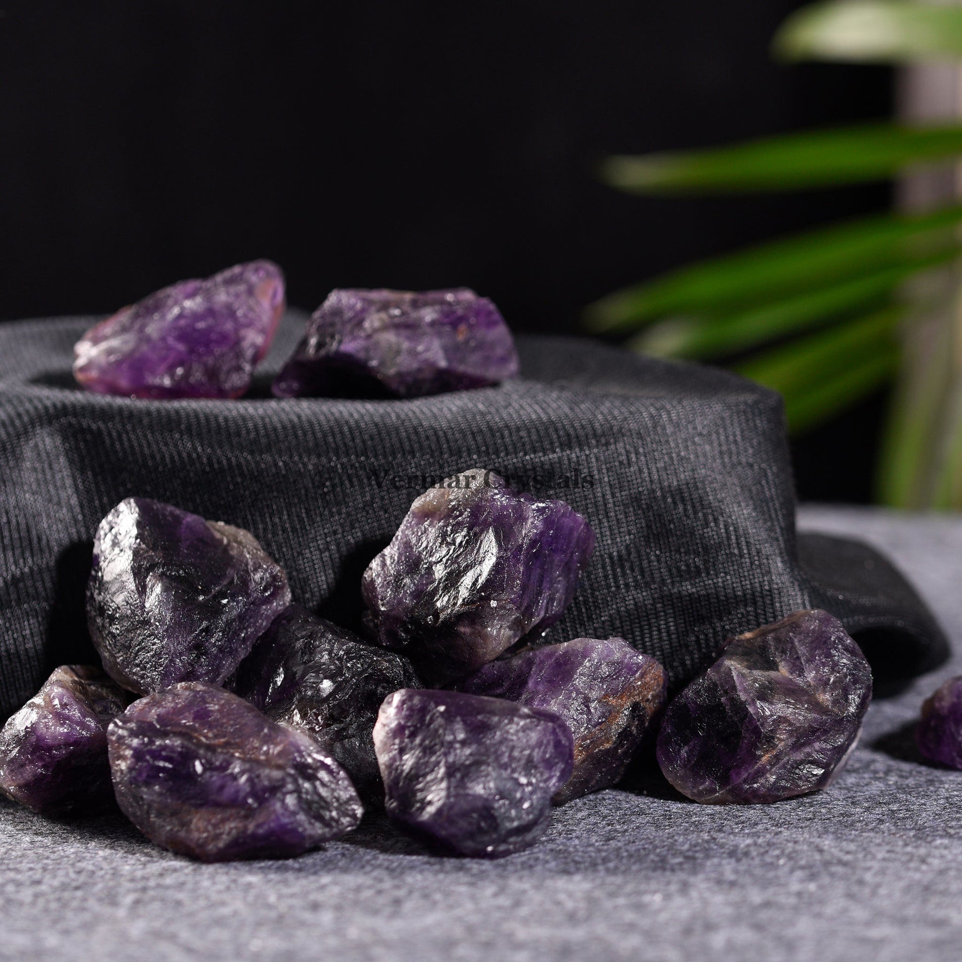 Natural rough Amethyst quartz stones with deep purple hues scattered on textured black fabric and gray surface