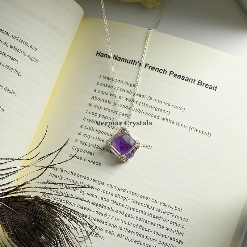 Handcrafted amethyst raw crystal pendant wire wrapped in silver, hanging on a delicate silver chain over an open cookbook page