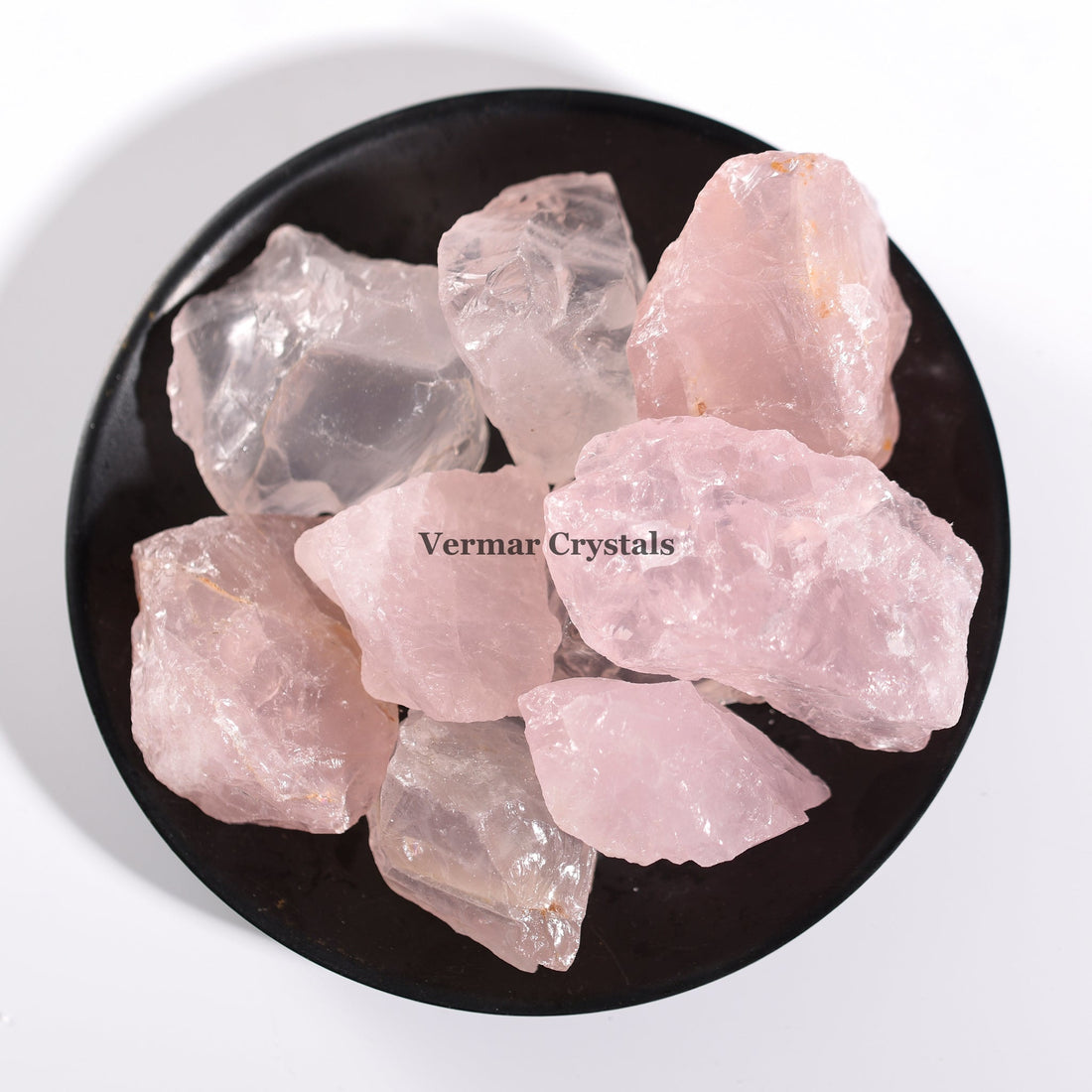 Natural rose quartz crystal stones in soft pink hues arranged on a black dish against white background