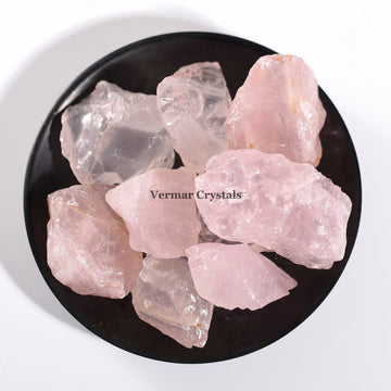 Natural rose quartz crystal stones in soft pink hues arranged on a black dish against white background