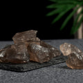 Natural smoky quartz crystal stones with rough, translucent brown surfaces displayed on a dark textured base