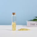 Mini glass vial filled with small yellow crystal chips sealed with a natural cork on white surface and blue background