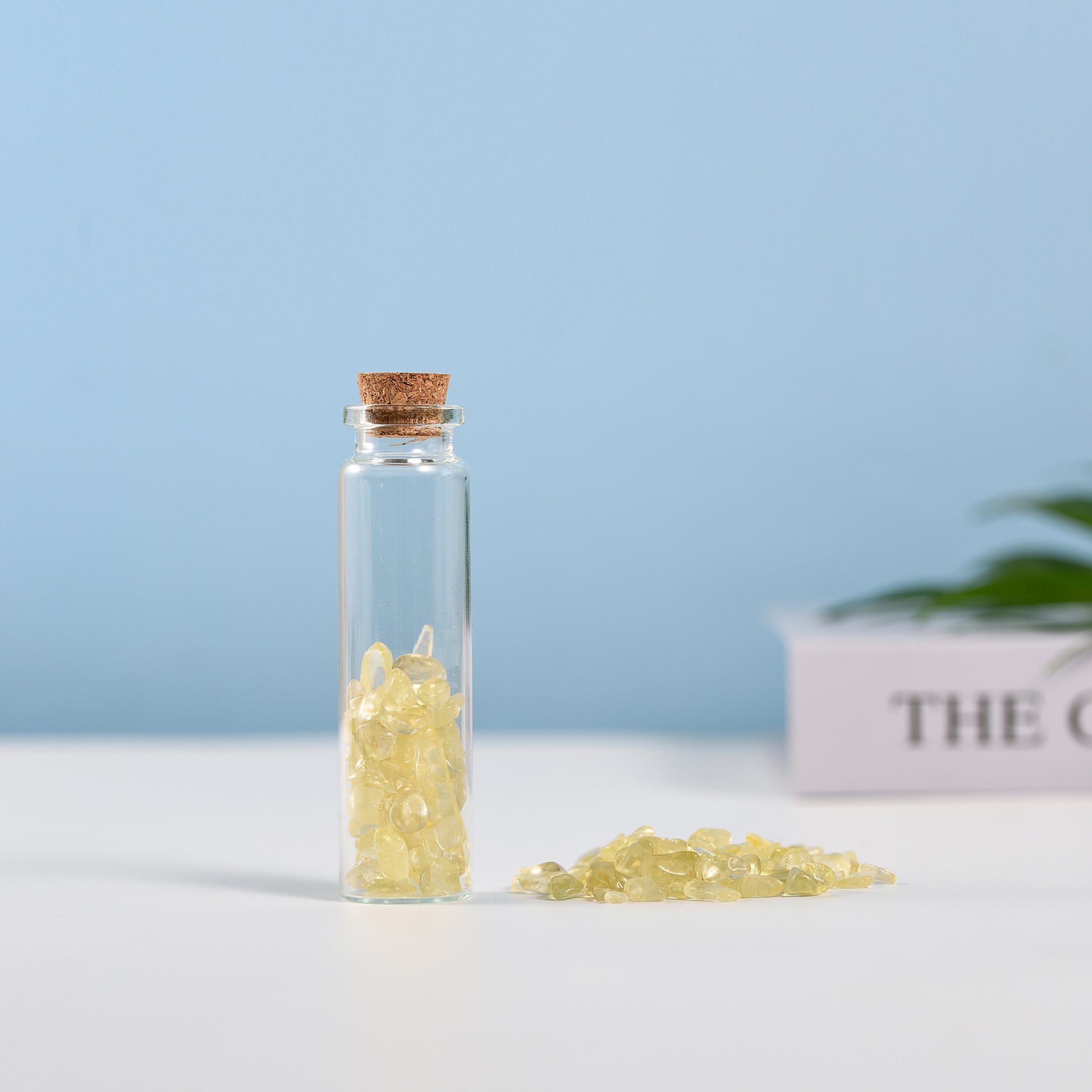 Mini glass vial filled with small yellow crystal chips sealed with a natural cork on white surface and blue background