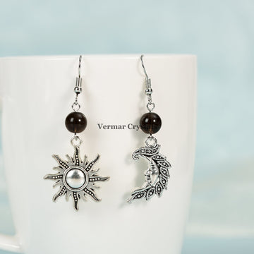 Asymmetric sun and moon earrings with smoky quartz beads and silver-tone metal charms hanging on white mug