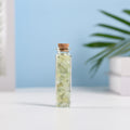 Mini glass vial filled with pale green natural crystal chips sealed with cork on white surface with soft background