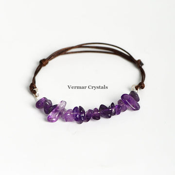 Handmade bracelet with irregular polished purple amethyst chip beads woven on an adjustable brown leather cord on white background