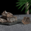 Collection of irregular smoky quartz crystal stones with translucent brown tones on a textured slate surface