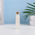 Mini glass vial filled with natural clear quartz crystal chips sealed with a cork on white surface and blue background