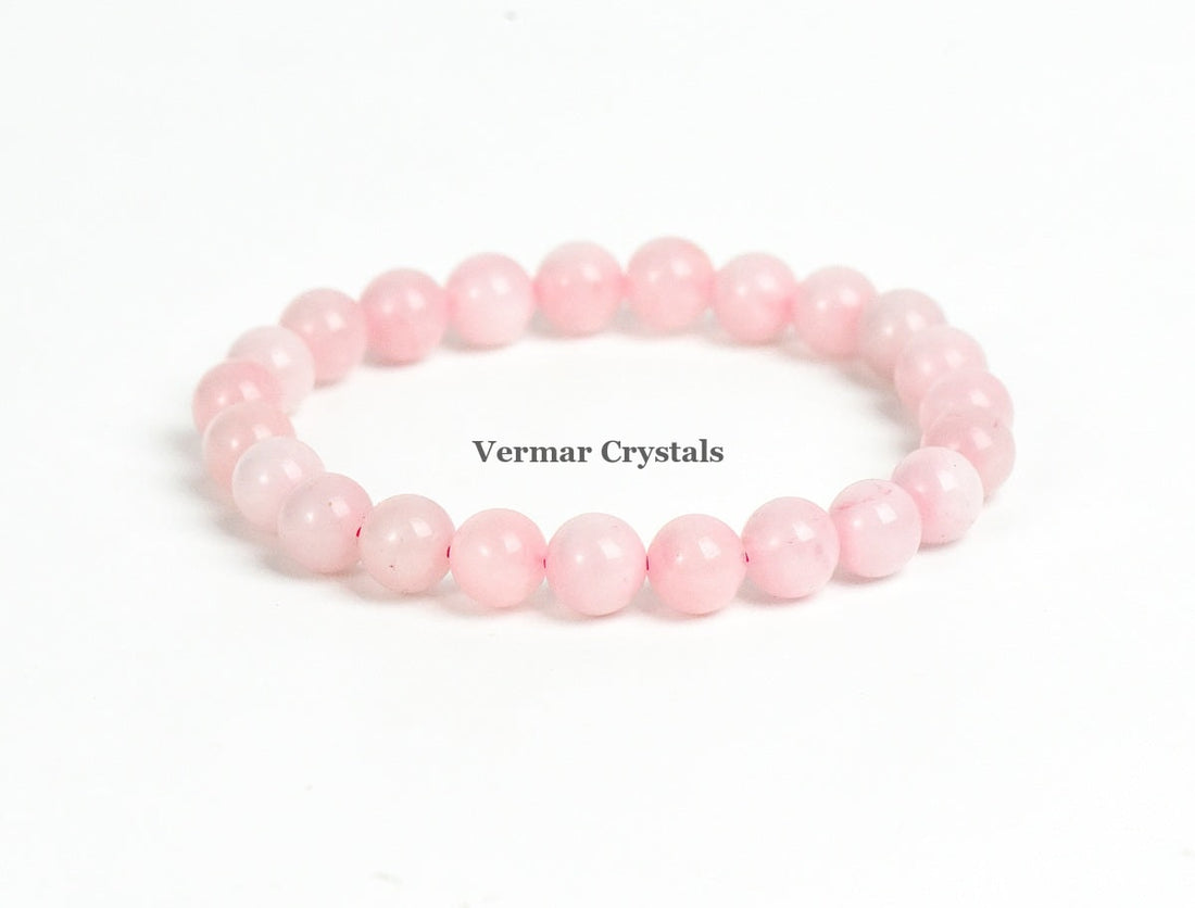 Stretchy bracelet made of smooth round light pink rose quartz beads arranged in a circle on a white background