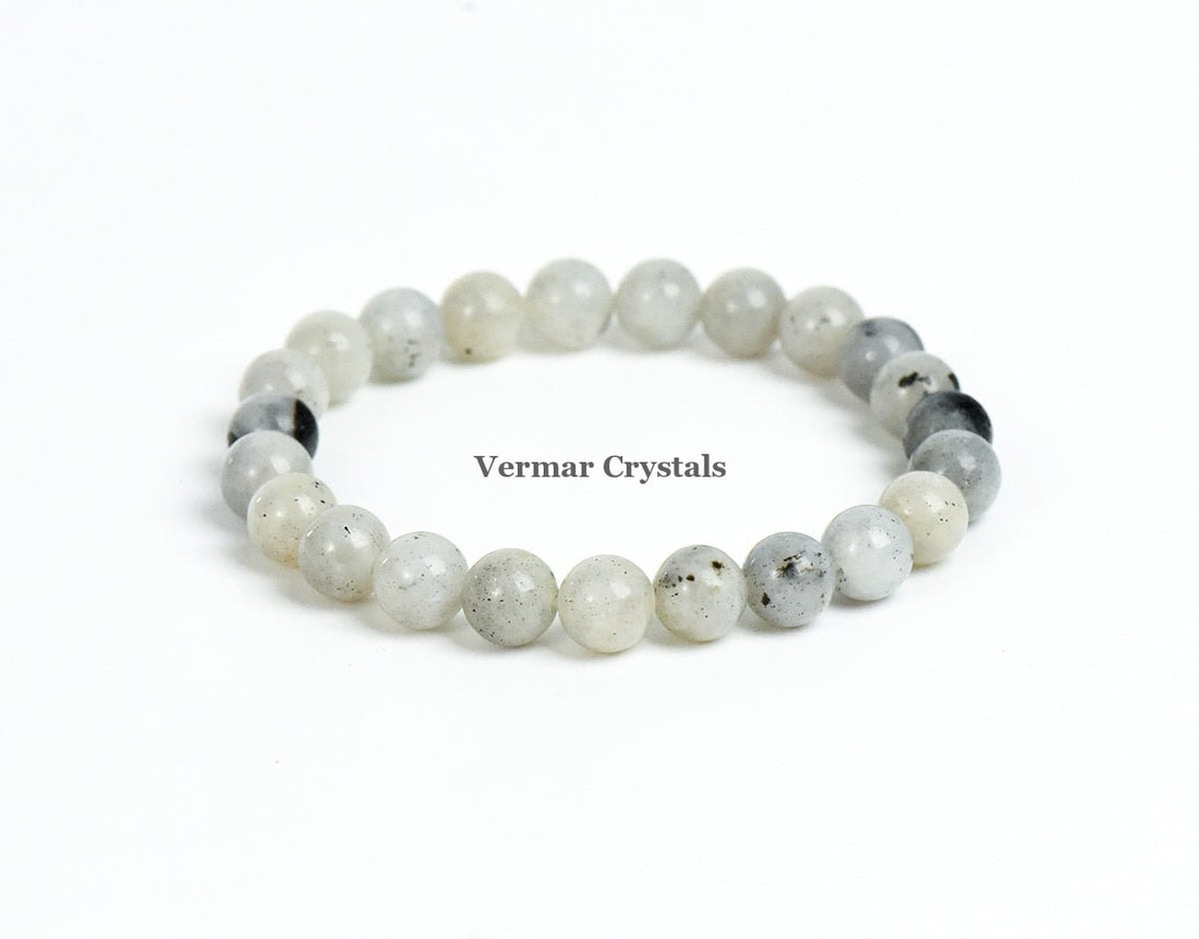 Stretchy bracelet made of smooth round pale gray and white labradorite beads arranged in a circle on a white background