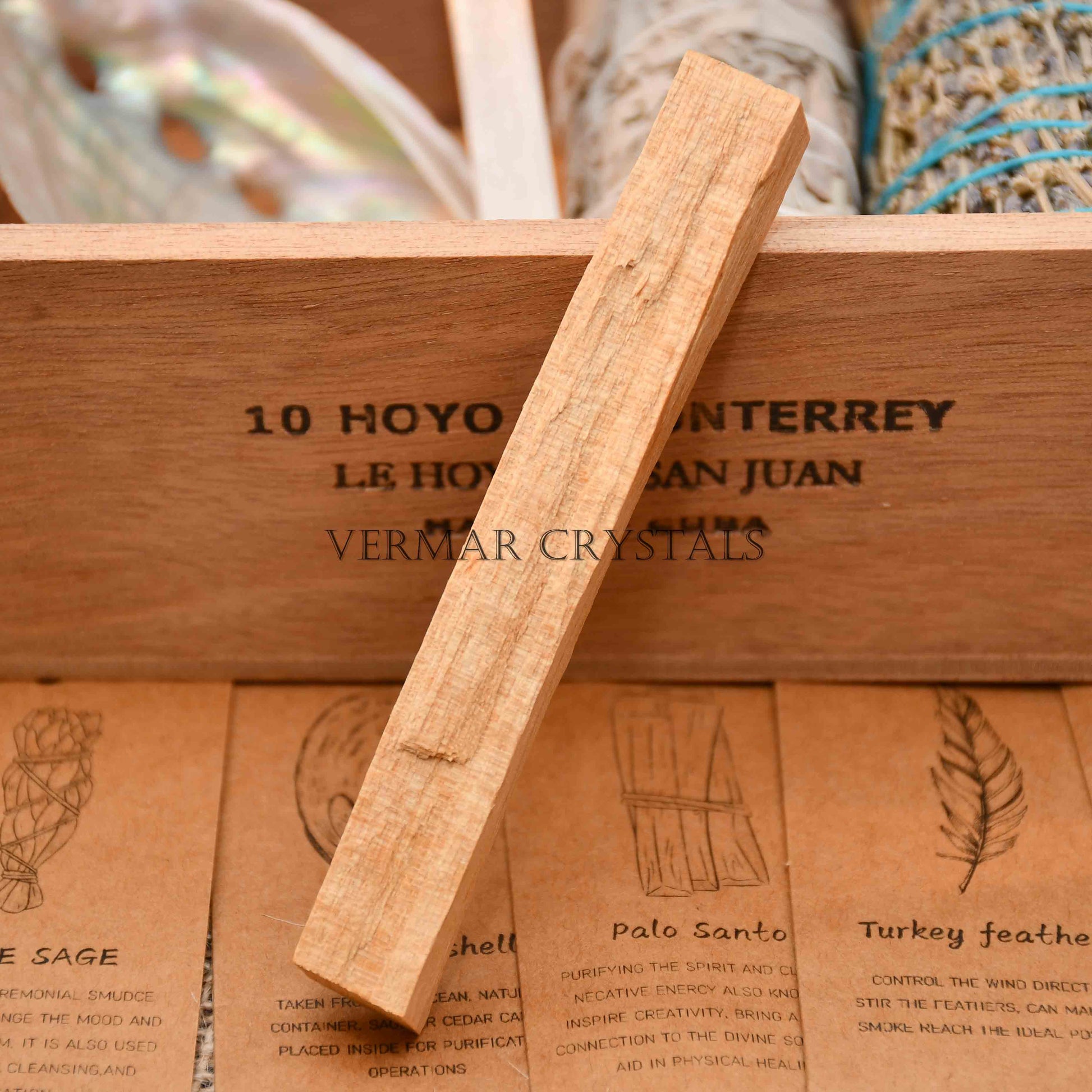 Single 10cm natural palo santo stick resting on wooden box with illustrated information cards below
