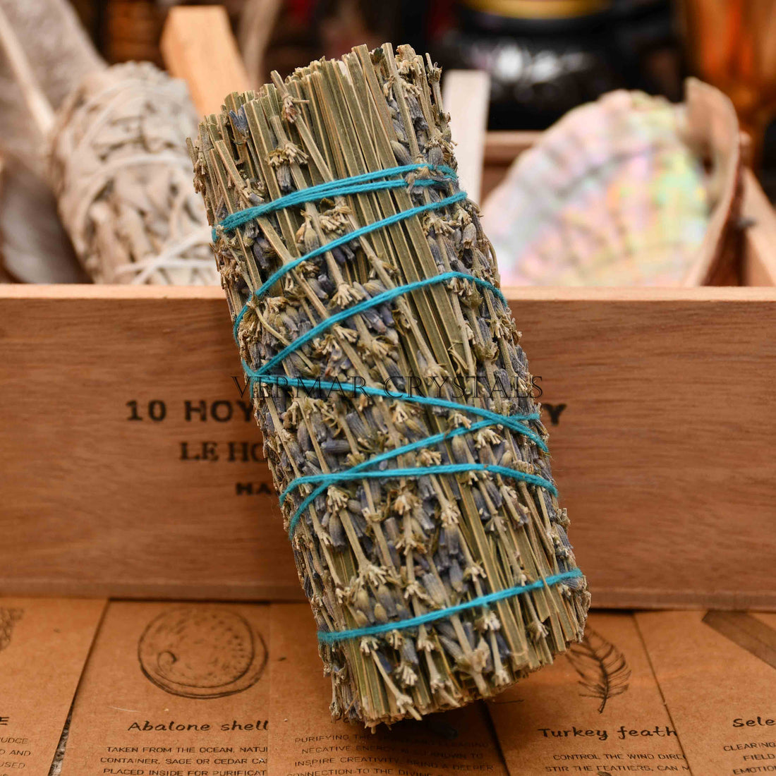 Hand-tied lavender smudge stick wrapped with turquoise string alongside a brown kraft paper tag on white background