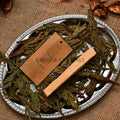 Natural Palo Santo stick on silver tray with green dried leaves and brown product information tag
