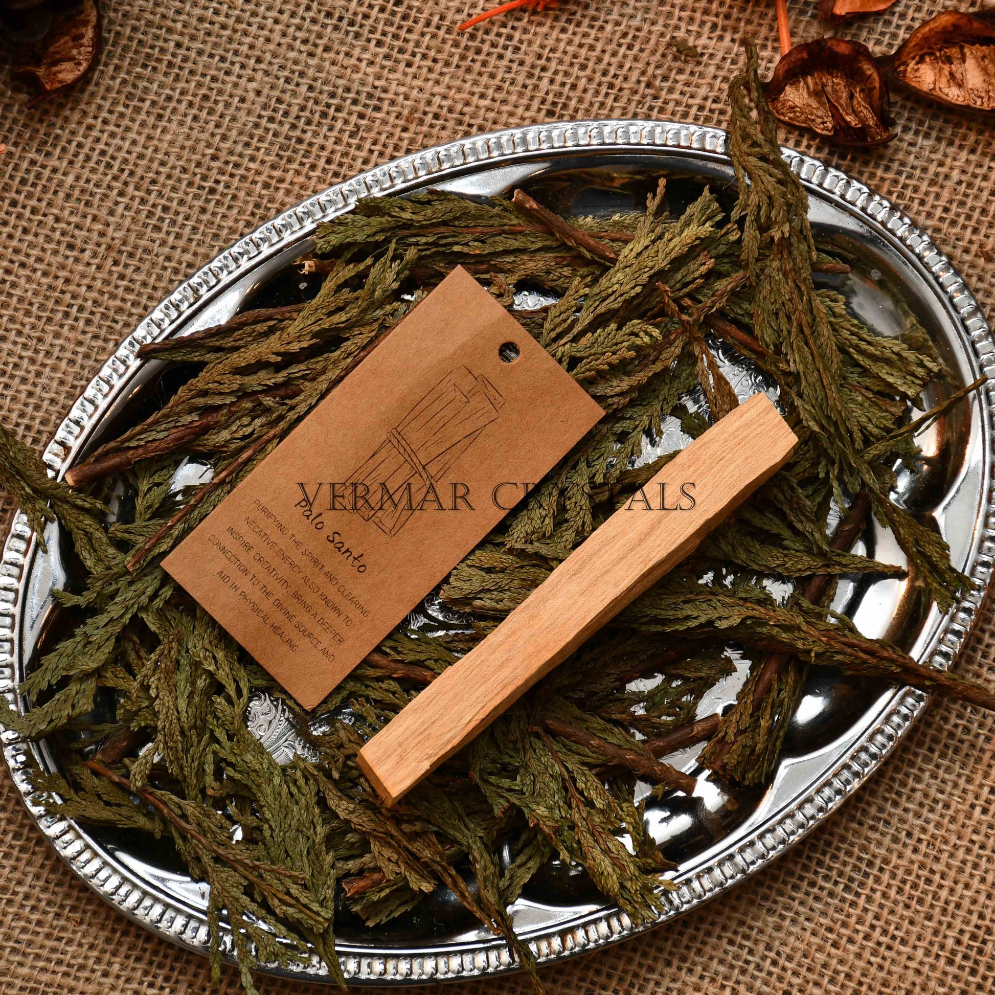 Natural Palo Santo stick on silver tray with green dried leaves and brown product information tag
