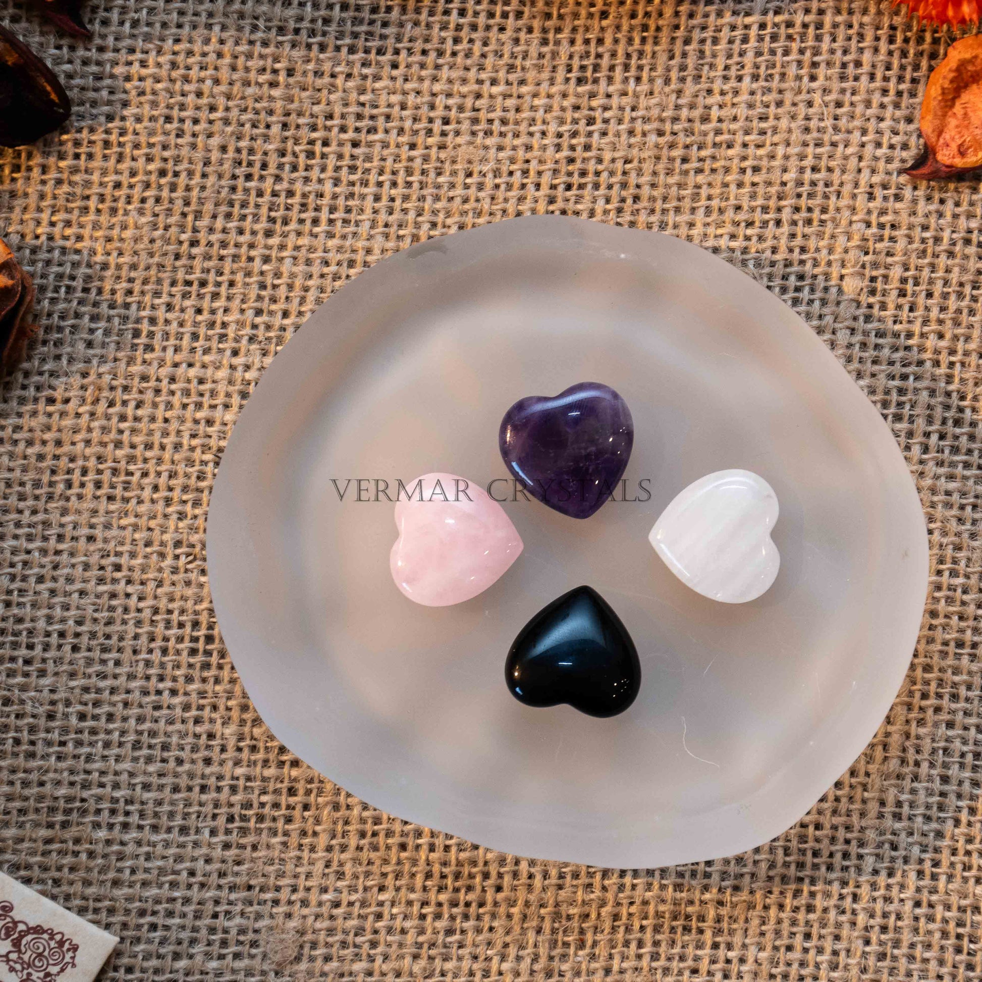 Four mini heart-shaped tumbled stones in amethyst, rose quartz, black onyx, and white selenite on a frosted dish