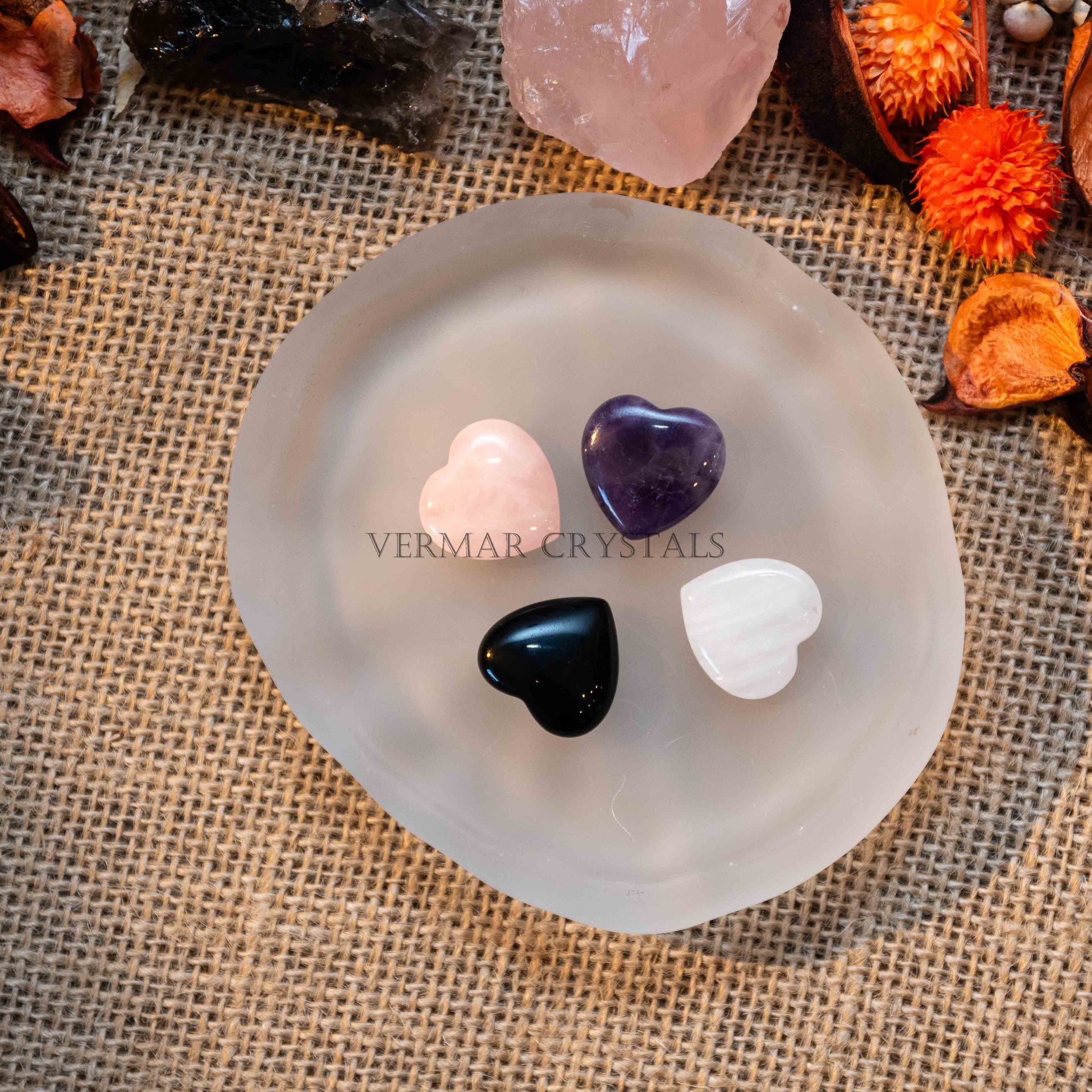 Four mini heart-shaped tumbled stones in various colors displayed on a smooth translucent dish on burlap background