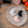 Three mini crescent moon-shaped tumbled crystals in clear quartz, rose quartz, and black obsidian on frosted glass dish