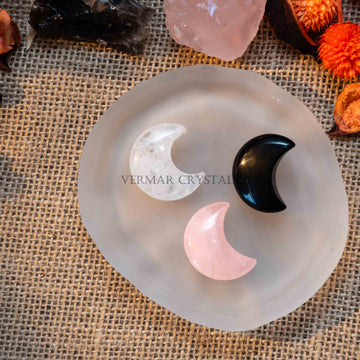 Three mini crescent moon-shaped tumbled crystals in clear quartz, rose quartz, and black obsidian on frosted glass dish