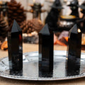 Three polished black obsidian towers standing upright on a decorative silver tray with blurred background objects