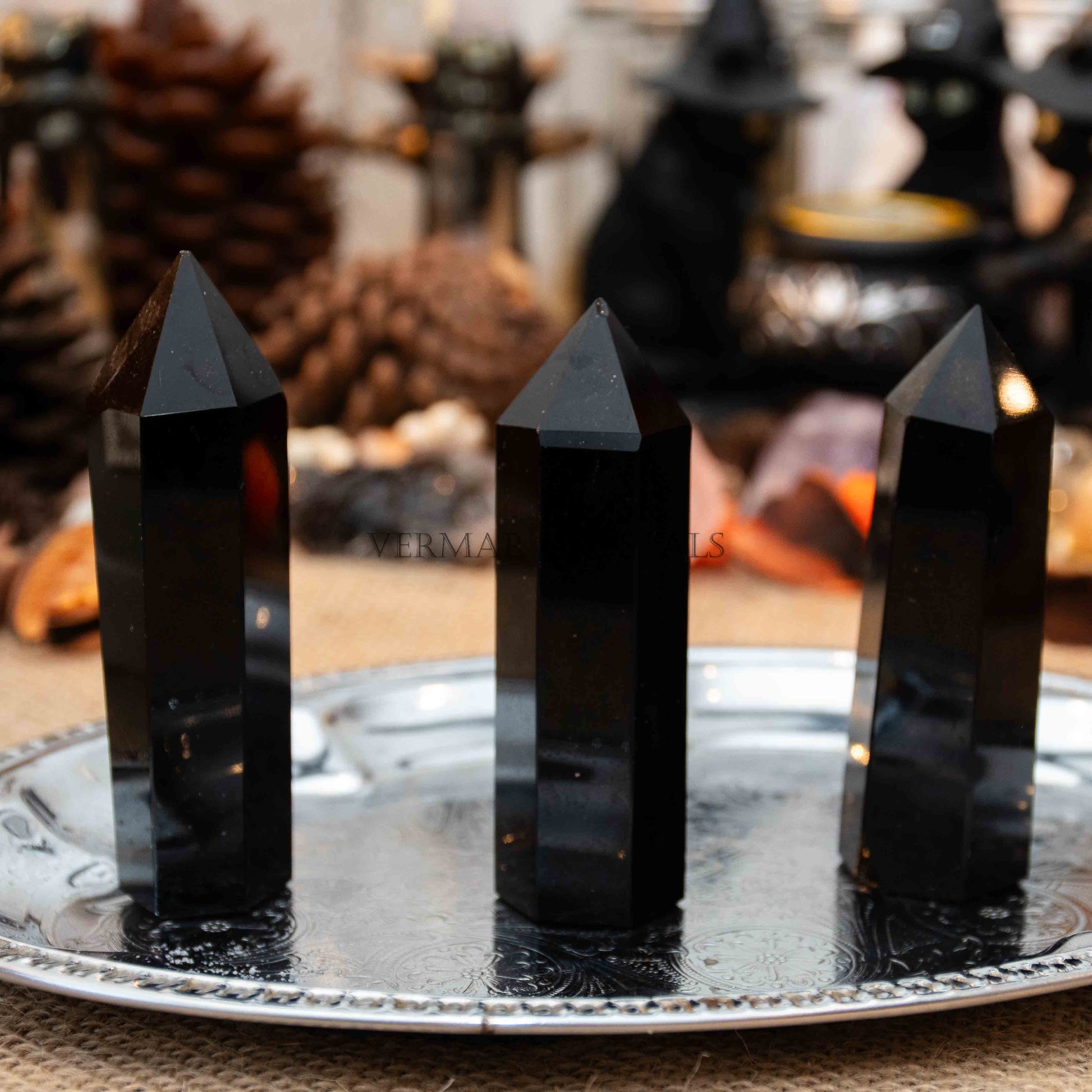 Three polished black obsidian towers standing upright on a decorative silver tray with blurred background objects