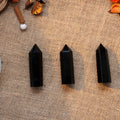 Three polished black obsidian towers standing upright on textured burlap with natural dried botanicals nearby