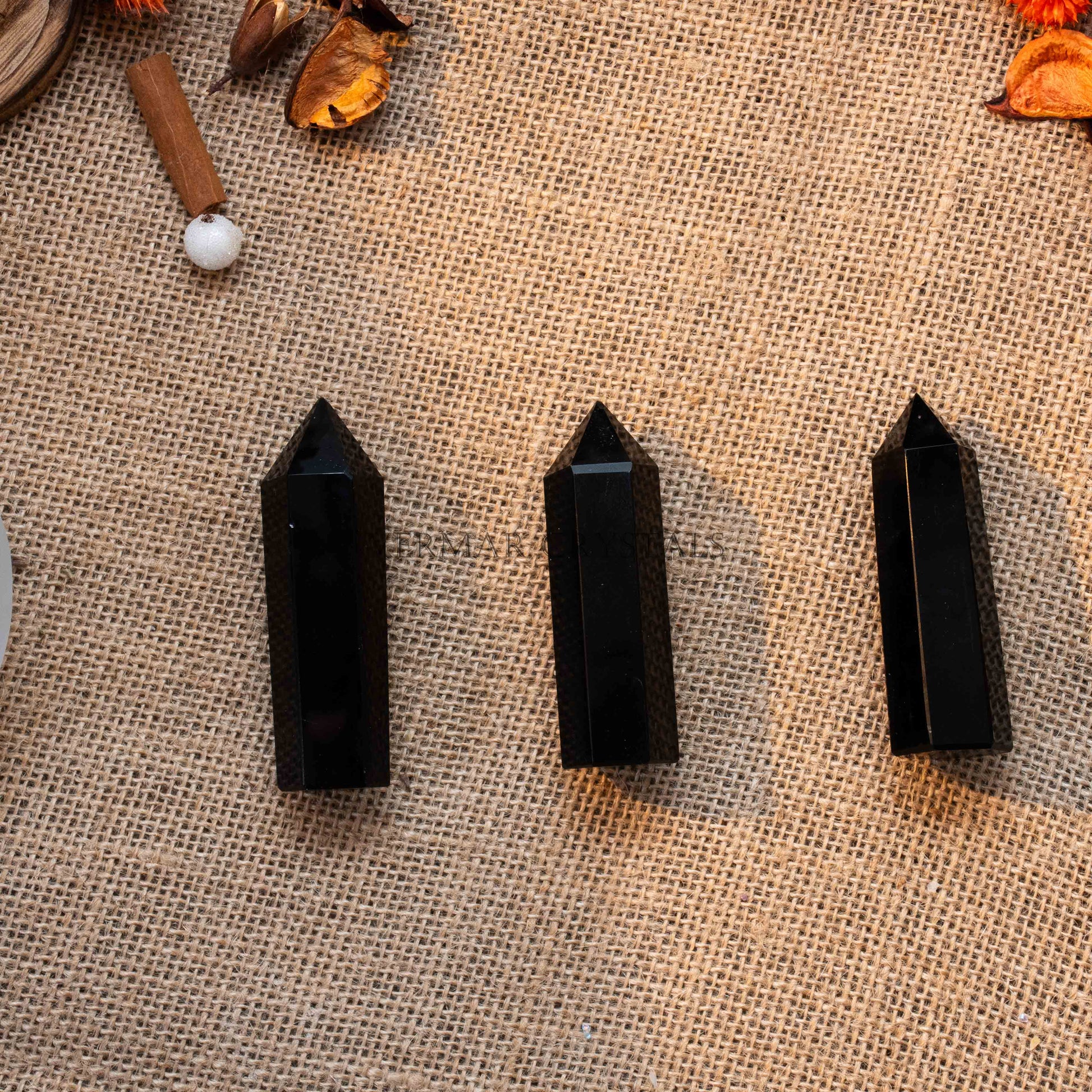 Three polished black obsidian towers standing upright on textured burlap with natural dried botanicals nearby