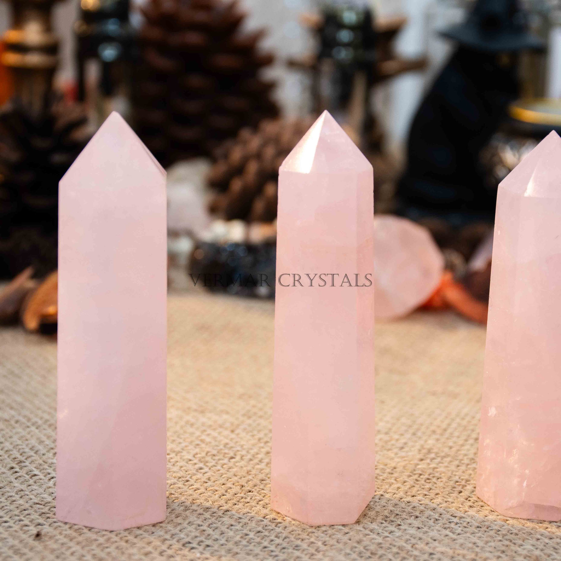 Three polished natural rose quartz towers standing upright on textured beige fabric with blurred background objects