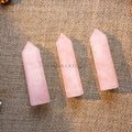 Three polished rose quartz towers with pointed tips displayed on a textured burlap surface