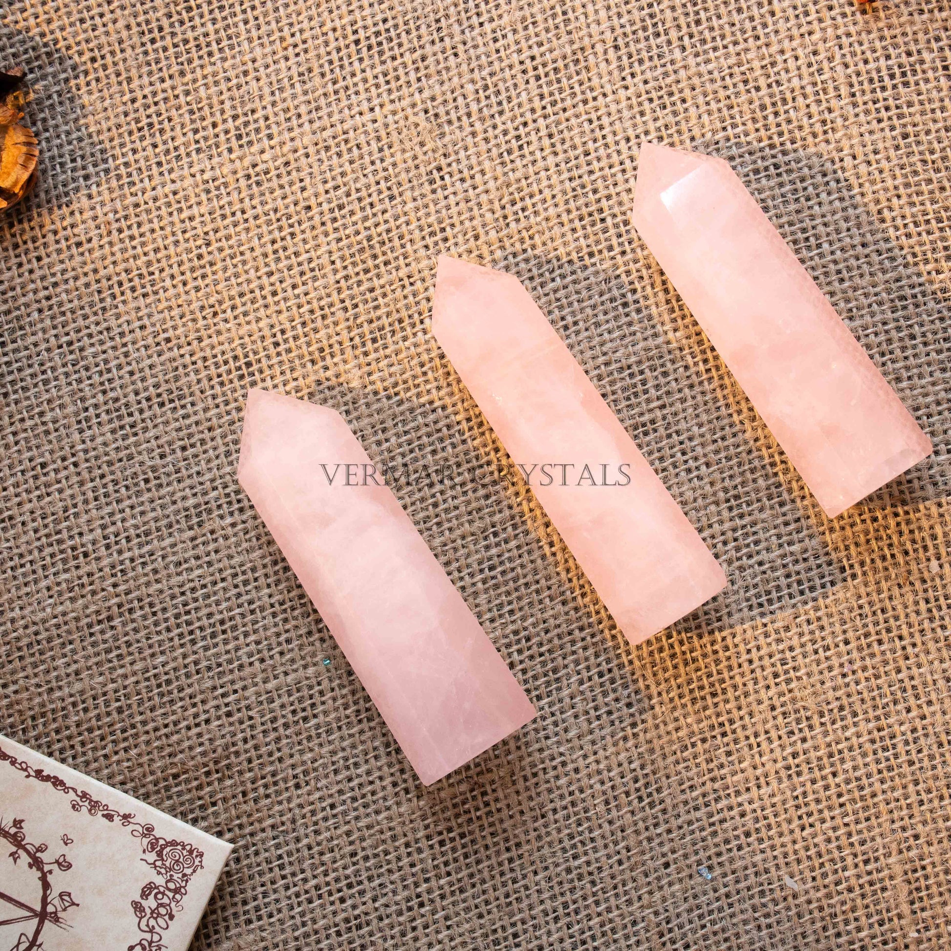 Three polished natural rose quartz towers with pointed tips on textured burlap surface