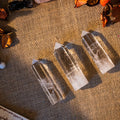 Three polished clear quartz towers with pointed tips on textured burlap fabric background with dried petals