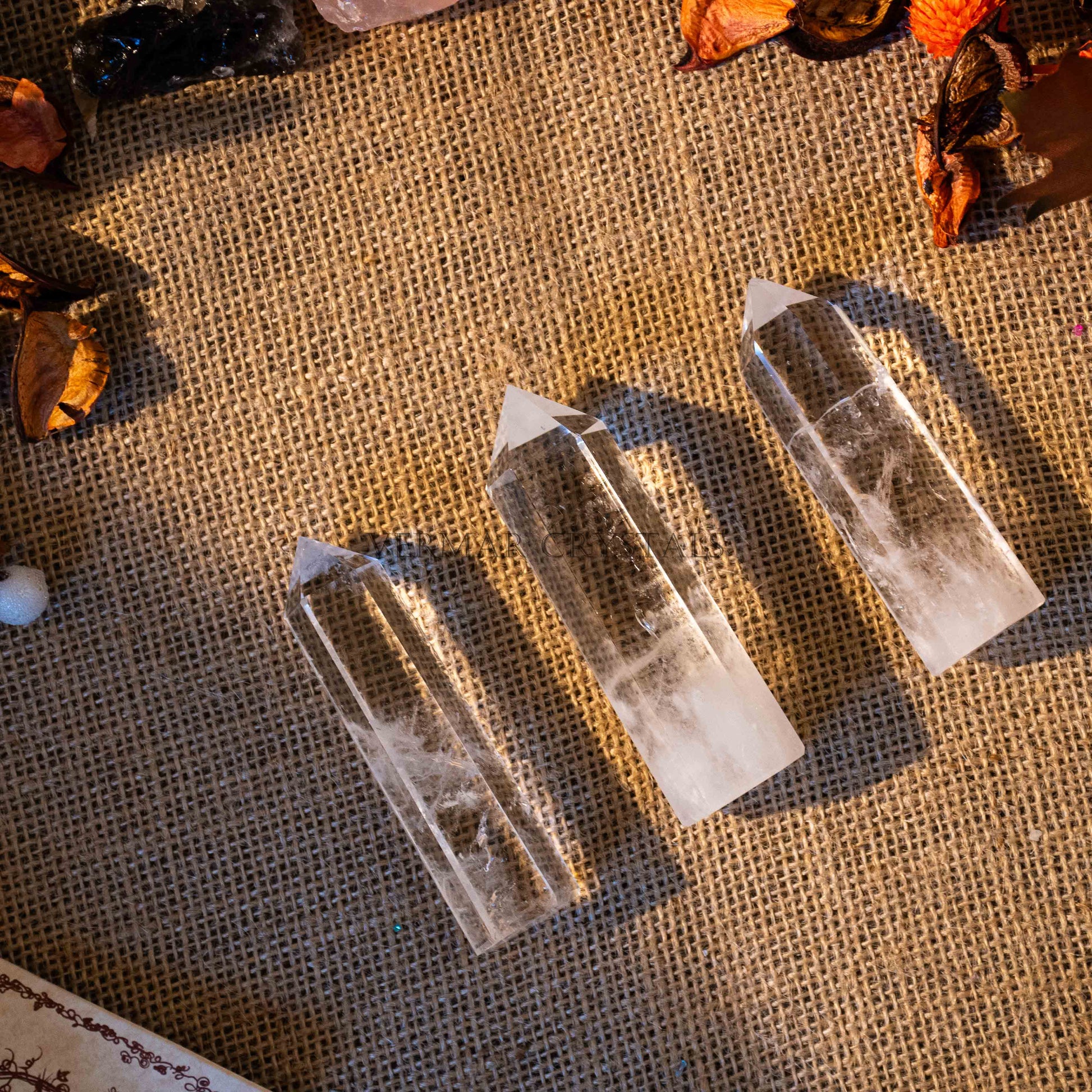 Three polished clear quartz towers with pointed tips on textured burlap fabric background with dried petals