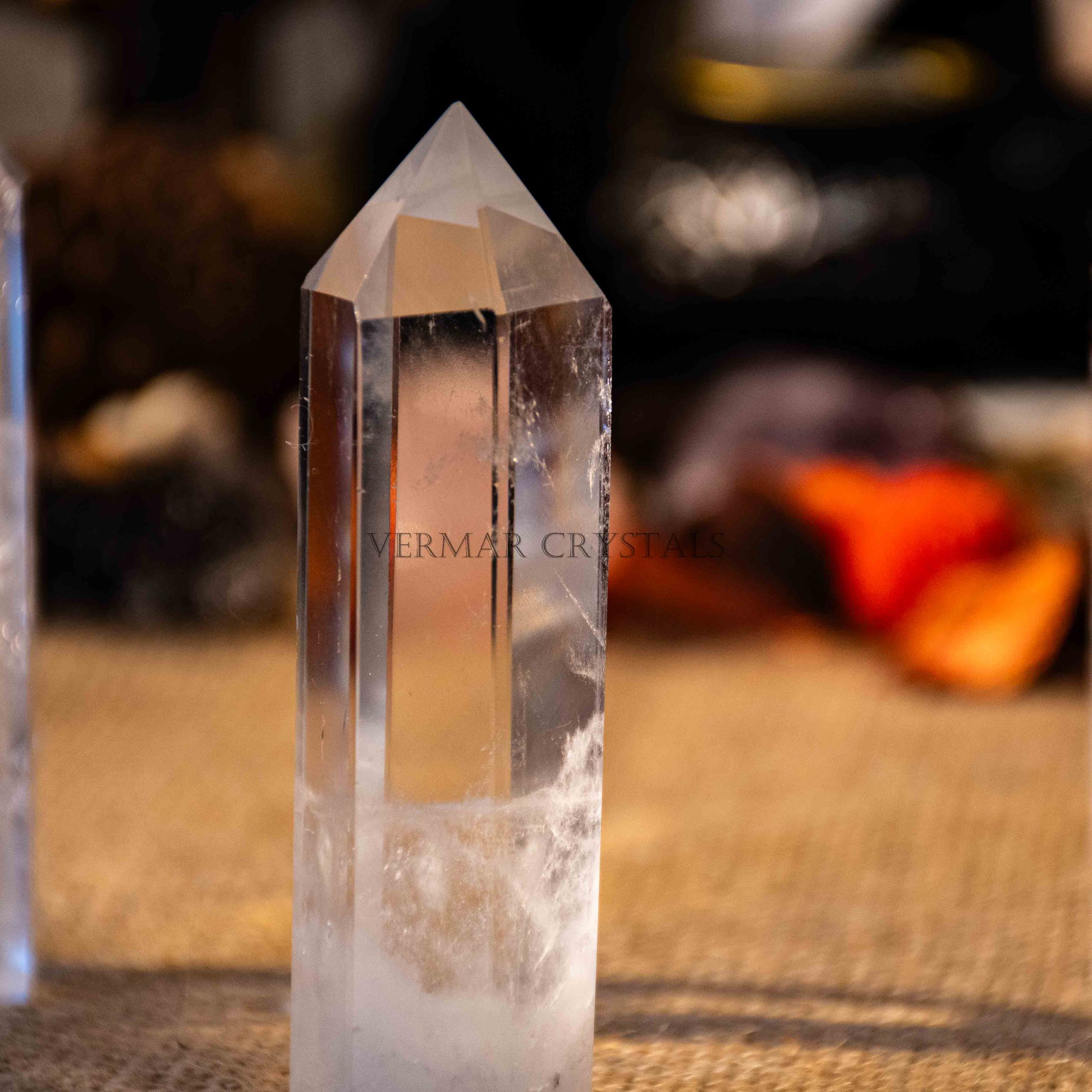 Clear quartz tower with a pointed tip and natural inclusions on textured surface with blurred background