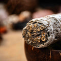 Close-up of premium white sage smudge stick wrapped tightly with natural twine resting on wooden bowl with blurred background