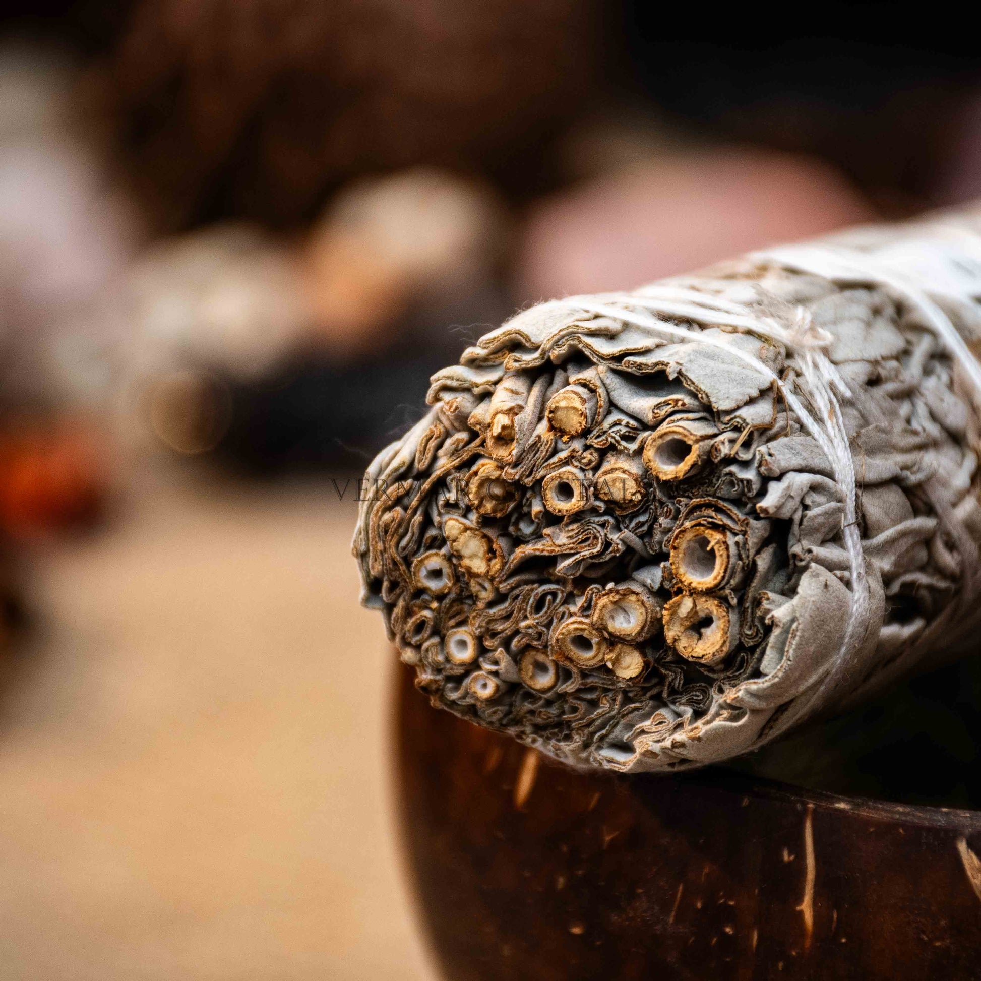 Close-up of premium white sage smudge stick wrapped tightly with natural twine resting on wooden bowl with blurred background